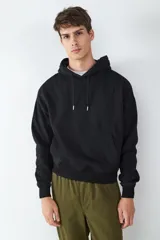 Buzo con capucha de color negro, con bolsillo tipo canguro frontal, mangas largas con puños elásticos y cordones ajustables en el cuello.