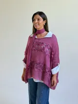 Sweater de punto magenta con diseño holgado, cuello redondo y detalles de encaje floral aplicado en el frente. Incluye una bufanda tipo choker integrada del mismo tejido.