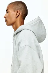 Campera con capucha de H&M, confeccionada en tejido pesado de mezcla de algodón con interior cepillado. Presenta un corte oversized, hombros caídos, cierre frontal completo, bolsillos tipo canguro y cordones ajustables en la capucha.
