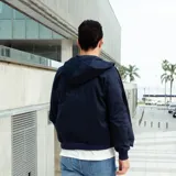 Campera azul marino de gabardina con capucha, cierre frontal con cremallera, puños y cintura acanalados y un pequeño logo bordado en el pecho.