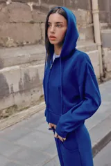 Sudadera azul con capucha ajustable con cordones, cierre frontal con cremallera, bolsillos delanteros de tipo canguro y manga larga.