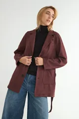 Chaqueta de gamuza sintética color bordó, con cuello solapa, cierre frontal de botones y cinturón ajustable del mismo material. Posee bolsillos frontales y mangas largas.