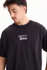 Remera negra de manga corta, confeccionada en algodón, con calce semi boxy y pequeño estampado frontal con la frase "away for a while".