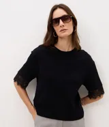 Remera de algodón blanca de corte recto, con cuello redondo, mangas cortas amplias y detalle de encaje aplicado en los puños.