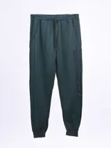 Pantalón deportivo de tejido tipo jogging color verde oscuro jaspeado, con cordón ajustable en la cintura y puños elásticos en los tobillos. Presenta bolsillos laterales y un pequeño detalle estampado verticalmente en el muslo derecho.