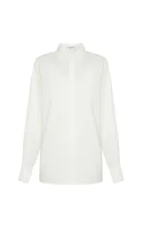 Camisa blanca de corte recto con cuello clásico estructurado, mangas largas con puños ajustados y cierre frontal de botones ocultos. Presenta un panel trasero con frunces y detalle elástico, con un bajo ligeramente redondeado.