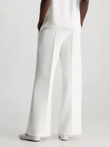 Pantalón blanco de pierna ancha confeccionado en tejido de punto técnico con poliéster reciclado y elastano. Presenta talle medio, pinzas delicadas en el centro de la pierna, bolsillos con ranura y barra de metal con logo de Calvin Klein debajo de la cintura.