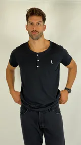 Remera tipo Henley de manga corta, color negro, con cuello redondo y cierre frontal parcial con tres botones. Presenta un pequeño logo bordado en el pecho.
