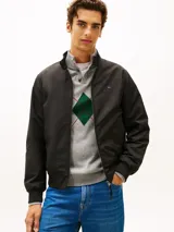 Campera tipo Harrington de Tommy Hilfiger en color negro, de corte amplio y tejido repelente al agua. Cuenta con cuello levantado, cierre frontal de cremallera con botón, bolsillos de ojal en la cintura, y puños y bajo de punto canalé. Presenta el logo de la marca bordado en el pecho.