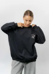 Buzo oversize de algodón frizado color negro, con cuello redondo, puños y cintura tejidos. Presenta un bordado pequeño de Snoopy en el frente.