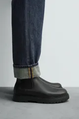 Bota tipo Chelsea de cuero color marrón oscuro, con paneles elásticos laterales, tirador trasero y suela track con volumen.