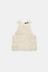 Top corto de cuello halter, confeccionado con una estructura de tejido que forma flores en relieve por toda la prenda. Presenta cierre en la espalda con abertura y botón oculto.
