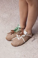 Zuecos de cuero color beige, con cordones marrones y verdes, y detalles de costuras.