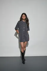 Vestido corto de denim azul oscuro, con cuello camisero, mangas cortas, cierre frontal de botones y dos bolsillos en el pecho.