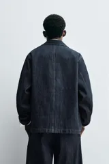 Chaqueta de denim de algodón en color azul oscuro, con corte relajado, cuello solapa, manga larga y cuatro bolsillos frontales con solapa. Presenta cierre frontal oculto por solapa.