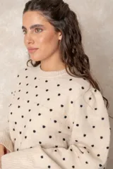 Buzo de punto color beige con estampado de lunares negros en relieve, cuello redondo y mangas largas con puños acanalados.
