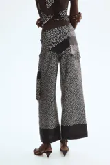 Pantalón negro con estampado de lunares blancos, corte recto y falda cruzada superpuesta con lazada en el lateral.