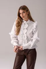 Camisa celeste con volados decorativos en los hombros, pecho, mangas y ruedo, destacados con ribetes en tono rojo. Presenta cierre frontal de botones, cuello alto y mangas largas abullonadas con puños ajustados.