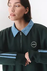 Buzo estilo rugby de corte oversized, color verde oscuro, con cuello tipo camisa en denim azul claro y cierre frontal parcial. Presenta un recorte horizontal en el pecho, logo bordado y tiras laterales en las mangas en contraste.