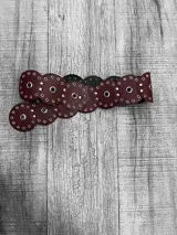 Cinturón ancho de cuero color borgoña con apliques circulares metálicos.
