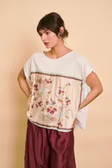 Blusa blanca de corte holgado, con mangas cortas y un panel frontal de seda con estampado botánico y floral en tonos rosados, bordó y verdes.
