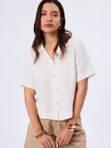 Camisa de manga corta color blanco, confeccionada en mezcla de viscosa, poliamida y lino, con cuello camisero y cierre frontal de botones.