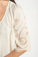 Blusa color arena de algodón peinado, con escote redondo, mangas cortas abullonadas con bordados suizos y detalles de alforcas en el frente.
