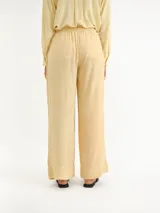 Pantalón de corte ancho, color amarillo claro, con cintura elástica fruncida y cordón ajustable. Cuenta con bolsillos frontales aplicados y dobladillo ancho en los tobillos.