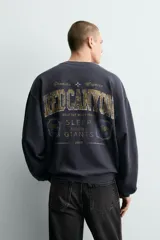 Sudadera de manga larga, cuello redondo y corte cropped, color azul marino oscuro con efecto lavado. Presenta un estampado frontal en tonos dorados y desgastados con el texto "RED CANYON" y las palabras "Granite" y "Majesty" flanqueando un símbolo de cruz.