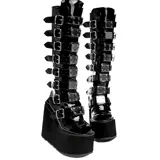 Botas de caña alta en charol negro con plataforma elevada. Presentan múltiples correas horizontales con hebillas metálicas y placas decorativas plateadas a lo largo de toda la caña.