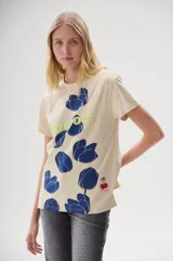 Remera color crema con estampado de flores azules y texto "Blossom" en verde.