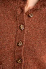 Cardigan de lana color marrón, con cuello alto, cierre frontal de botones y dos bolsillos delanteros. Presenta puños y ruedo acanalados.