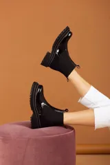 Botas tipo chelsea de cuero negro con textura granulada, paneles laterales elásticos y suela track robusta de goma.