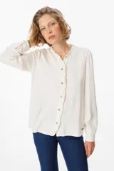 Camisa de manga larga color azul, con cuello mao y detalle de volados en la botonadura frontal. Presenta puños abotonados y un corte recto y fluido.