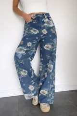 Pantalón de jean corte wide leg con estampado floral en tonos azules, verdes y blancos. Presenta tiro alto, diseño de pierna amplia y bolsillos traseros.