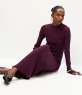Vestido midi de punto acanalado color bordó, con cuello redondo y mangas largas. Presenta un diseño ajustado en el torso que se extiende hacia una falda con caída fluida.