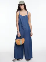 Enterito de denim suave confeccionado en 100% lyocell, con escote recto y breteles finos regulables que se ajustan en la espalda. Presenta una silueta amplia de pierna recta, caída fluida, bolsillos traseros aplicados y costuras a contratono.