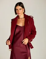 Chapaqueta estilo biker color bordó, confeccionada en tejido de lana con hombros estructurados y mangas largas. Cuenta con solapas amplias, cierre frontal cruzado, bolsillos con cremallera, detalles metálicos dorados y un cinturón integrado con hebilla a tono en el dobladillo.