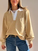 Buzo tipo chomba de corte oversize con diseño a rayas horizontales celestes y blancas. Presenta cuello camisero blanco y un bordado en la espalda con la inscripción República Oriental del Uruguay.