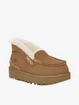 Mule de gamuza color tostado con forro de piel de oveja visible en el borde superior. Presenta costuras decorativas en contraste y una suela de plataforma dentada de goma.