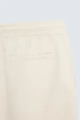 Bermuda de algodón color beige claro, de corte regular fit, con cintura elástica ajustable mediante cordón. Presenta bolsillos laterales y un bolsillo trasero de vivo.
