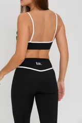 Conjunto deportivo de tres piezas compuesto por un top con breteles finos, una campera entallada con cierre frontal y una calza semioxford. Todas las prendas son de color negro con detalles de ribetes blancos en los bordes.