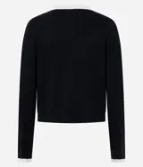 Cardigan corto de punto en color blanco con detalles en negro, cuello redondo, manga larga y cierre frontal de botones perlados con ribete negro. Cuenta con dos bolsillos delanteros de ojal con ribete negro y botón.