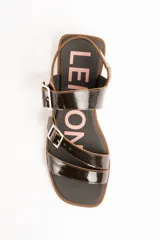 Sandalias de cuero charolado negro con dos tiras con hebillas metálicas plateadas y tira en el talón. Suela plana color marrón.