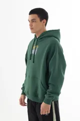Buzo hoodie verde oscuro con estampa serigráfica frontal de alta definición con una escena urbana en estilo puntillista y logo VERNAL con efecto dorado envejecido. Corte oversize con hombros caídos, capucha doble y bolsillo canguro.