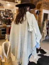 Ruana tejida en telar industrial de lana merino fina, con patrón geométrico en tonos gris y blanco, y terminación de flecos en los bordes.