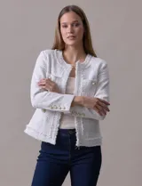 Chaqueta Nanette de tejido tweed color blanco, con escote mao, abertura central y bolsillos delanteros. Presenta apliques de botones perlados en los puños y terminación desflecada.