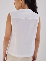 Camisa sin mangas de lino, color blanco, con cuello solapa, cierre frontal con botones y bolsillo pequeño en el pecho. Presenta costuras decorativas a la vista que definen la silueta.