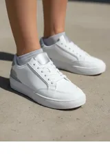 Championes urbanos de diseño minimalista en color blanco, con detalles en plateado brillante en la lengüeta y el talón. Presentan perforaciones laterales para ventilación y suela de goma al tono.