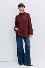 Sweater de punto con diseño de trenzas, cuello alto y mangas largas con puños acampanados. Presenta un corte holgado con terminación asimétrica en el ruedo.